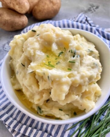 White bowl filled with mashed potatoes, melted butter, and chives.