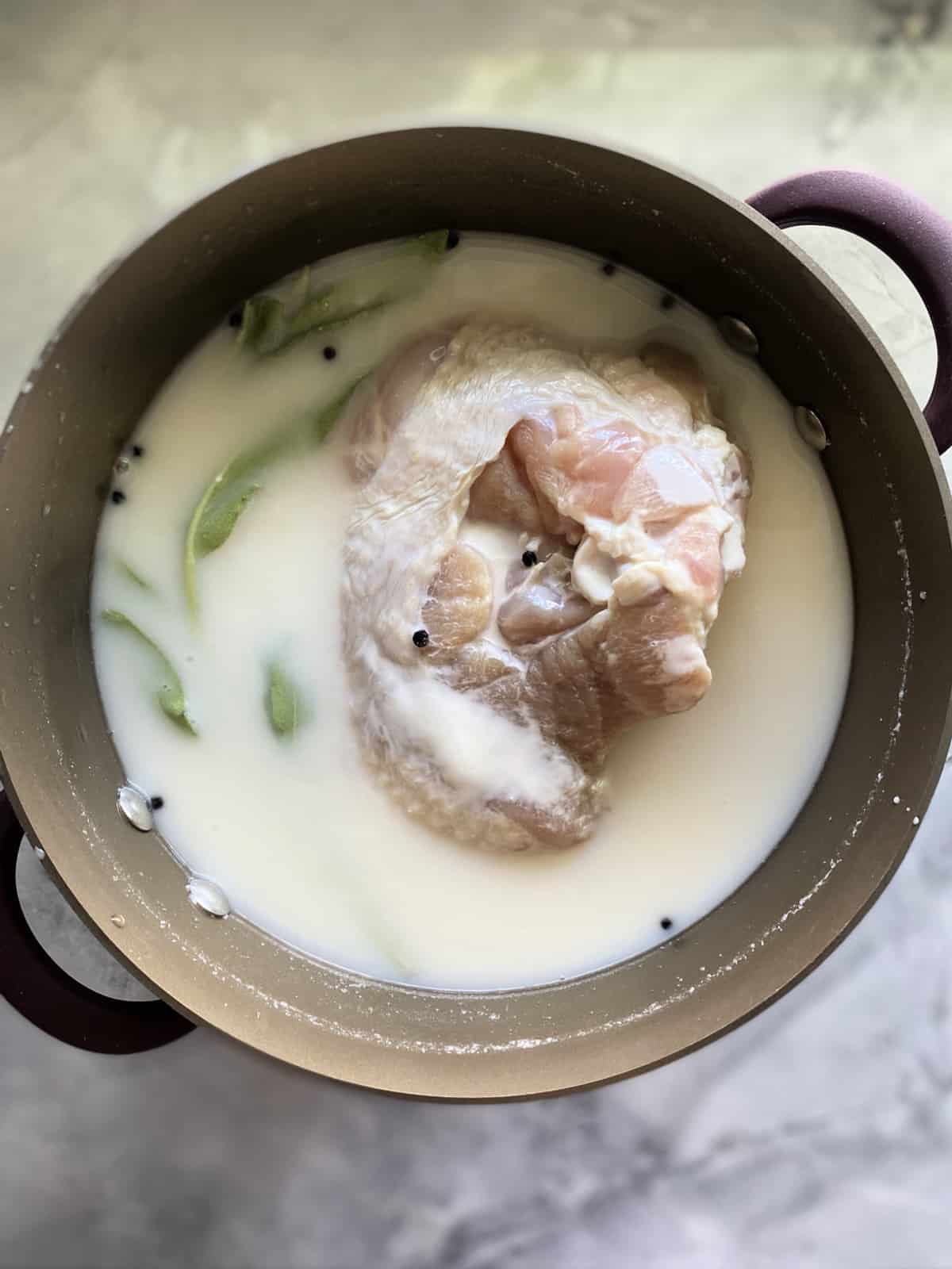 Top view of a pot filled with buttermilk, herbs, and raw turkey breast.