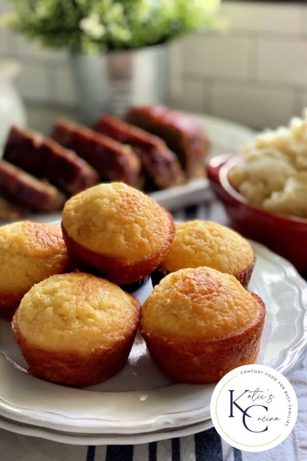 Cornbread muffins stacked on a two white plates with logo on the corner of photo.