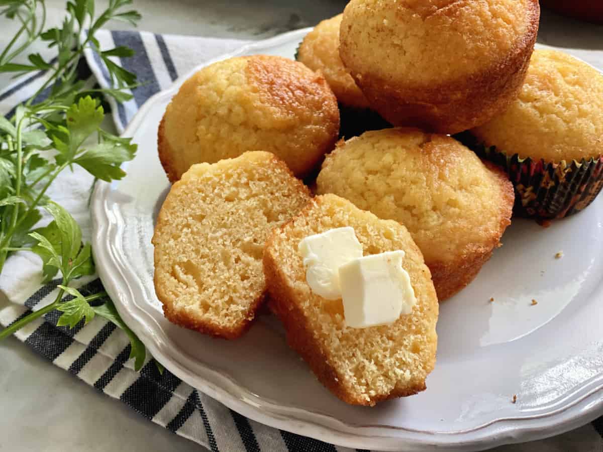 White plate with corn muffins stacked and one split with two squares of butter on it.