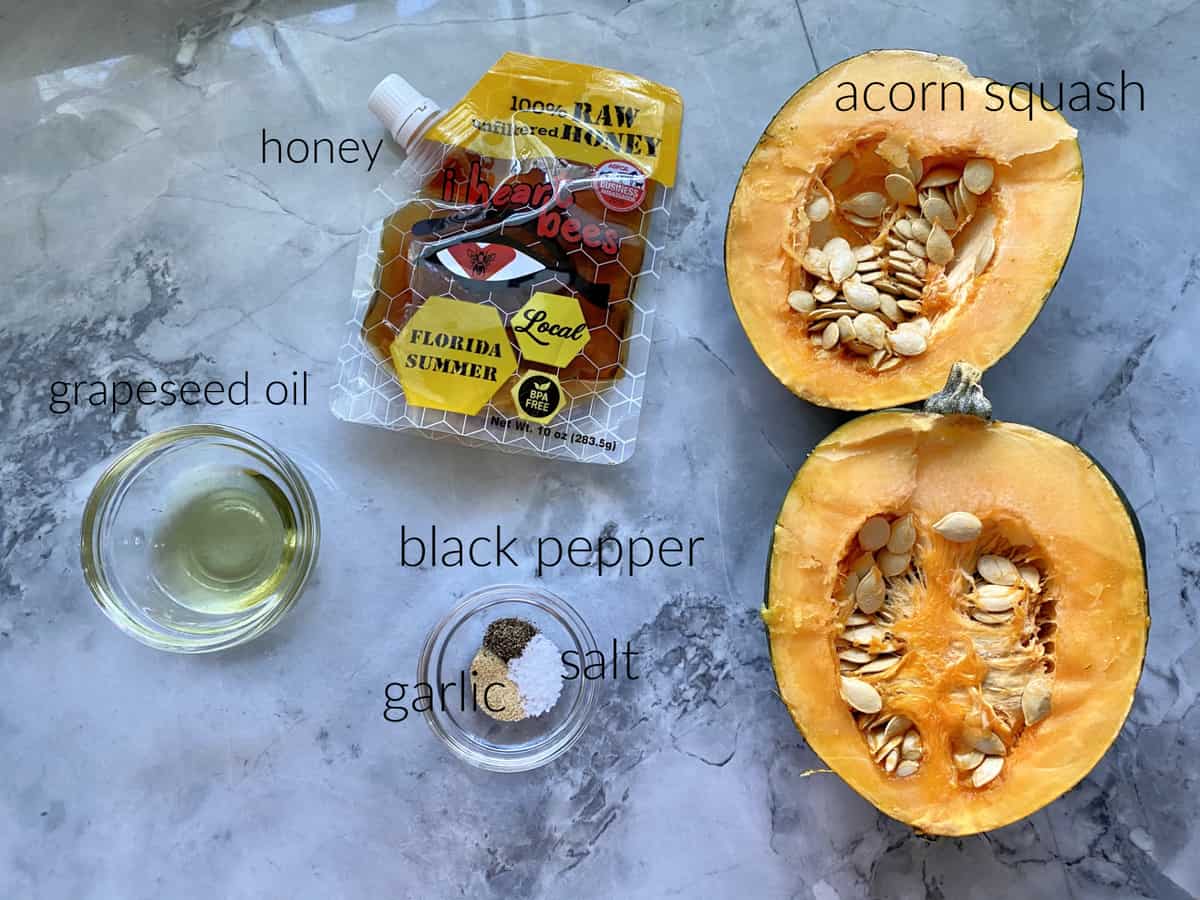 Ingredients: acorn squash, honey, grapeseed oil, seasonings on a marble countertop.