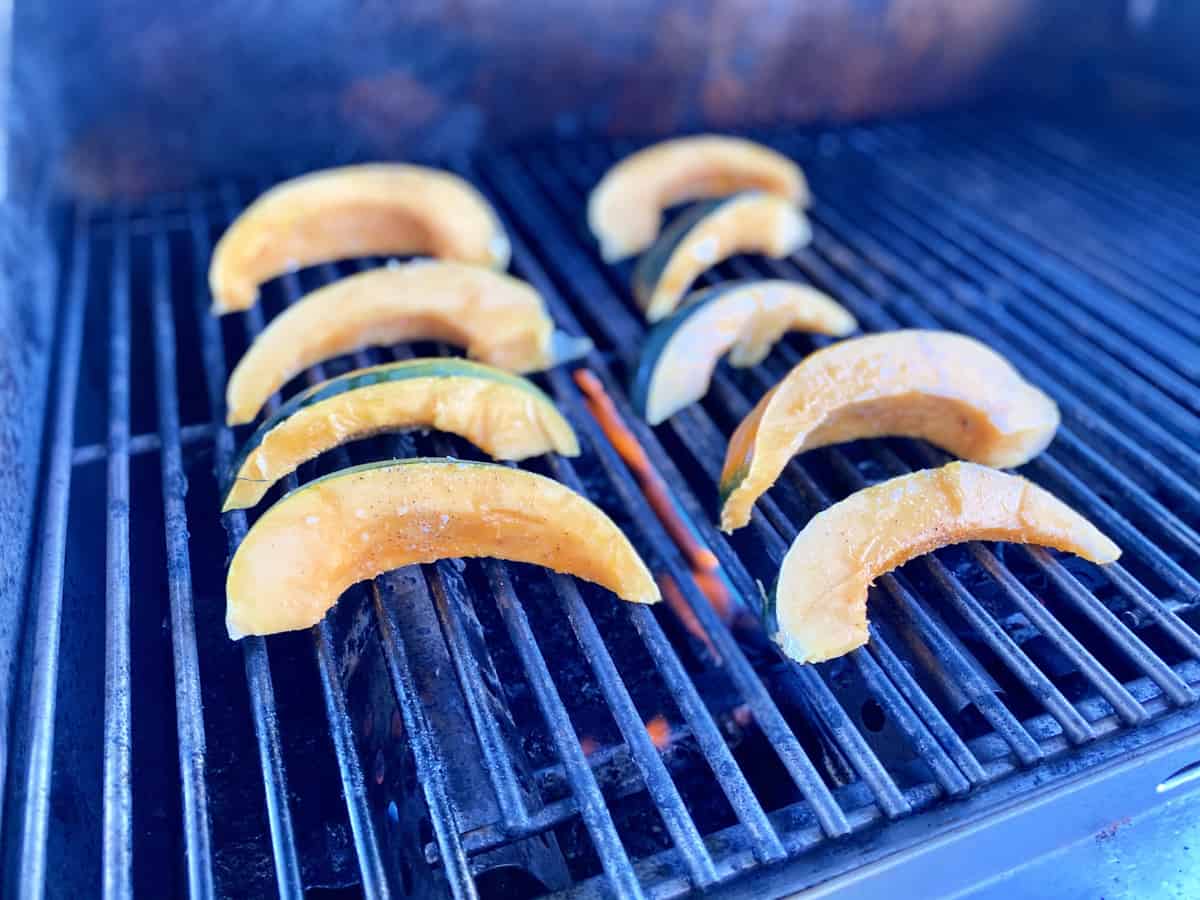 Sliced acorn squash cooking on a grill top.