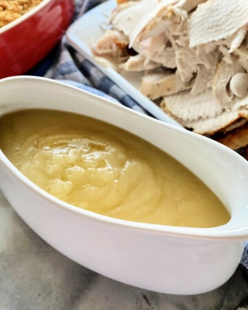 White gravy boat with yellow gravy inside and turkey in the background.