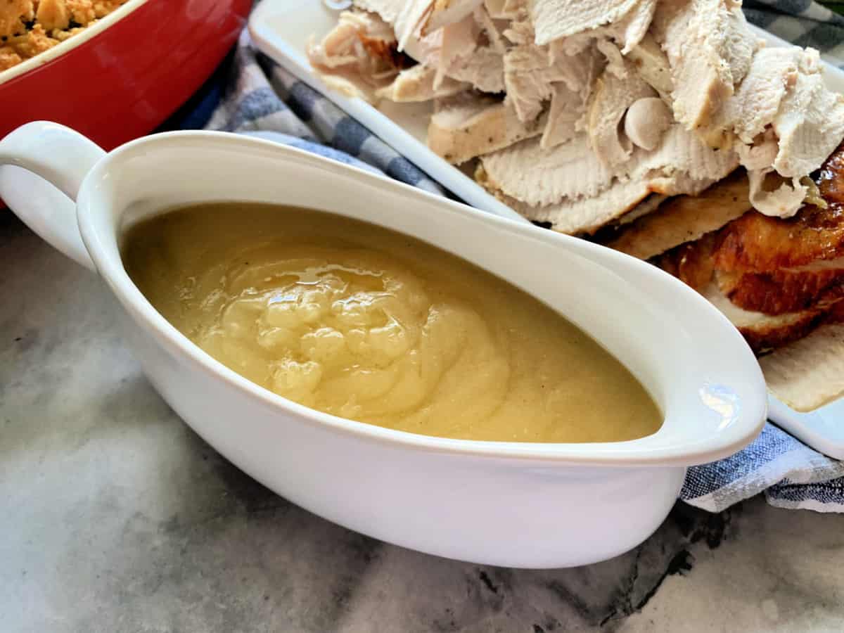 Turkey gravy in a white gravy boat with turkey breast sliced in background.