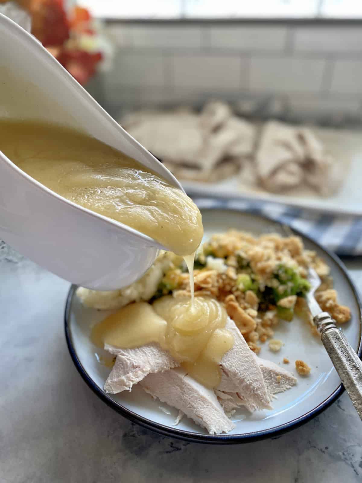 Gravy boat pouring gravy on top of sliced turkey breast.