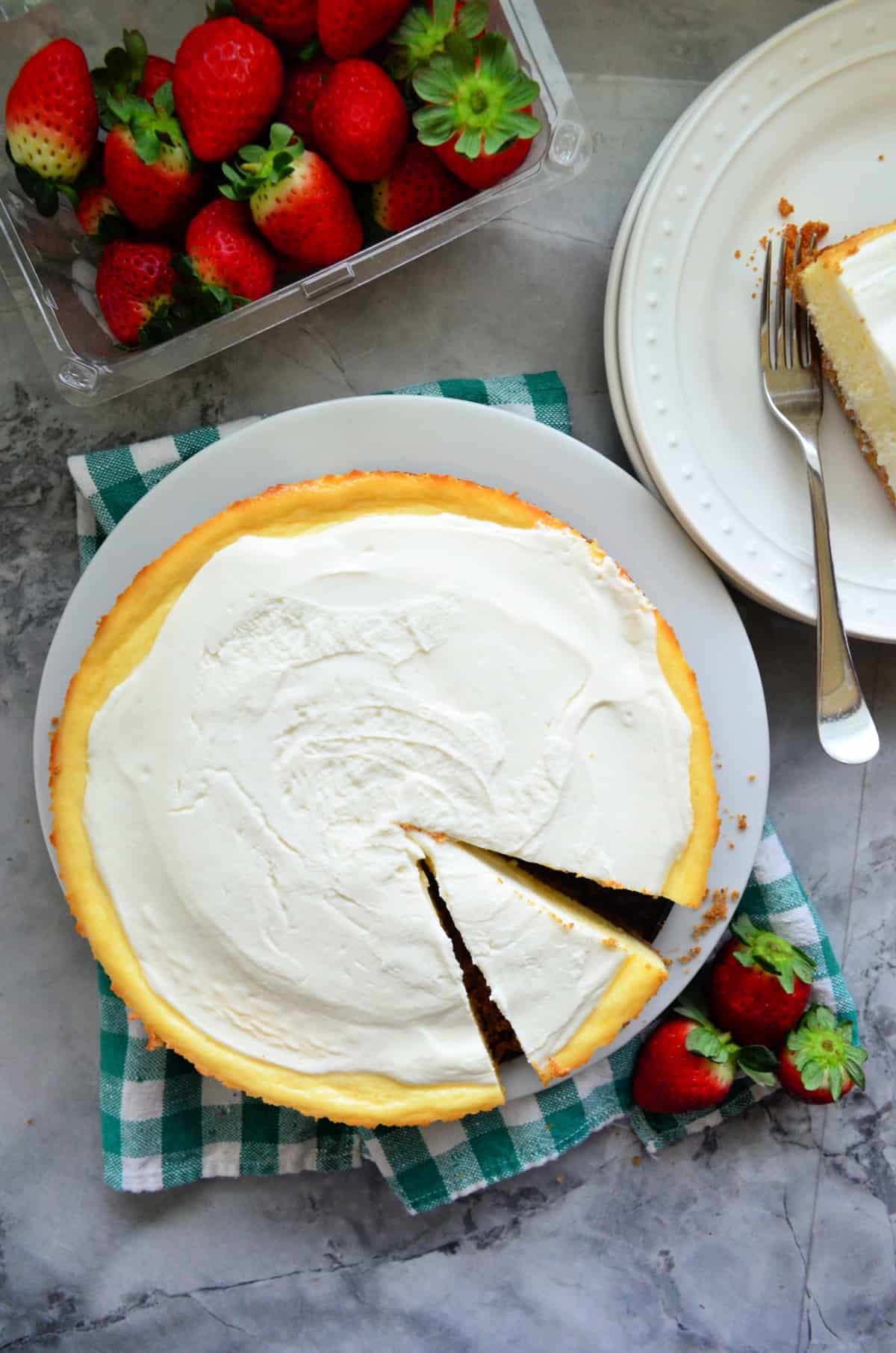 Top view of a sliced plain cheesecake with fresh strawberries on the side.