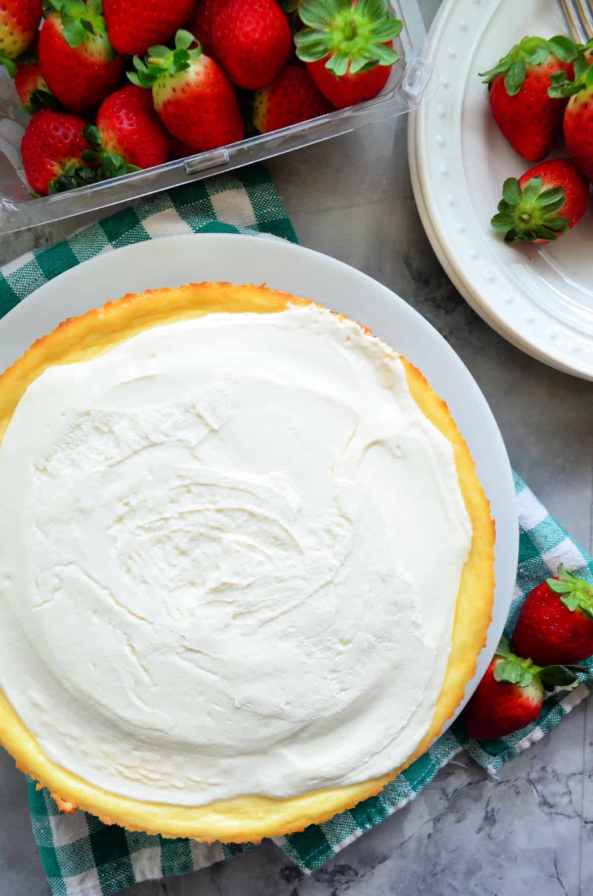 Top view of a whole cheesecake with a carton of fresh strawberries next to it.