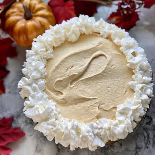 Full pumpkin cheesecake pie with fall leaves and pumpkins in background.