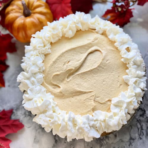 pie with whipped cream on marble countertop with leaves and pumpkins.