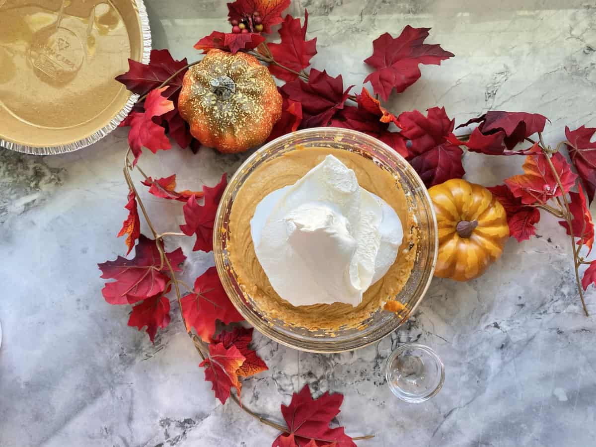 Glass bowl filled with pumpkin filling with whipped topping on top.