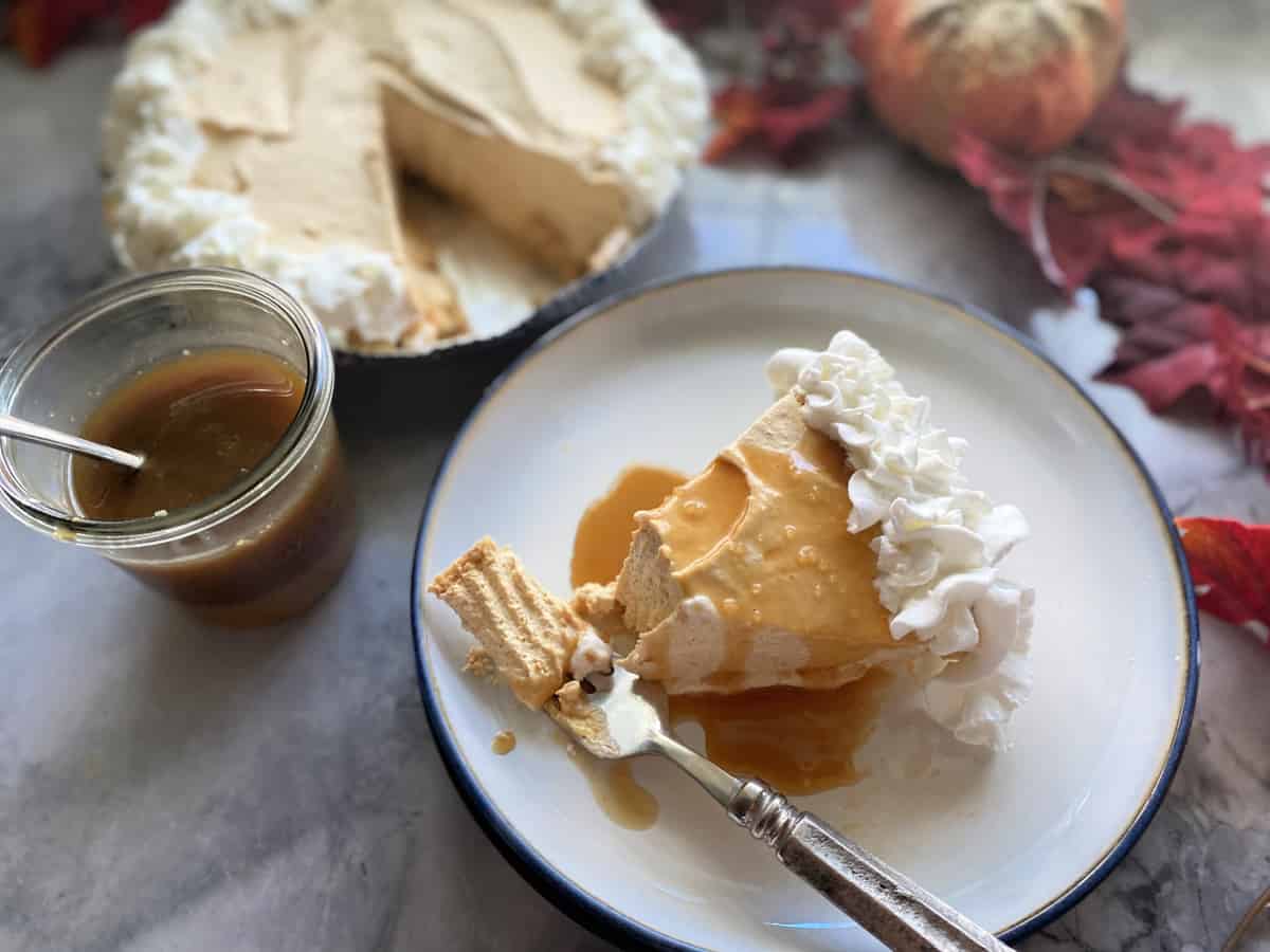 Slice of pumpkin cheesecake with fork bite and caramel sauce.