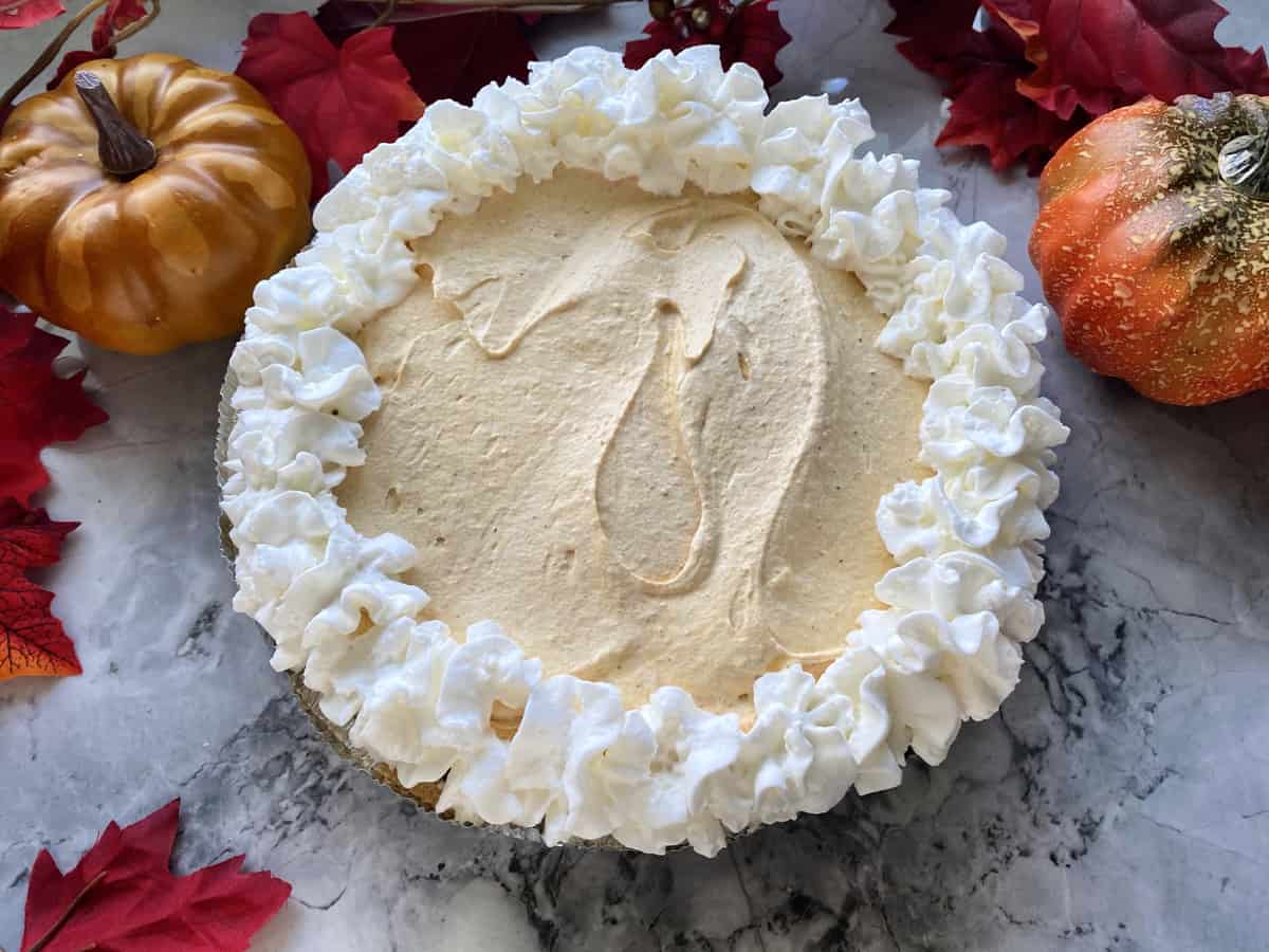 Pumpkin cheesecake pie with whipped cream topping and fall leaves around the edge.
