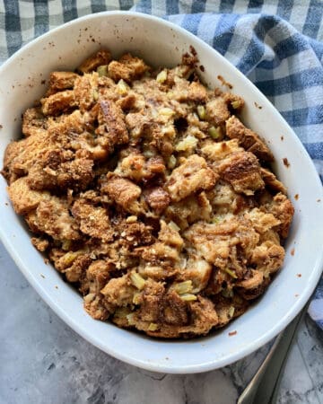 Top view of a white dish filled with bread stuffing resting on a plaid dish towel.