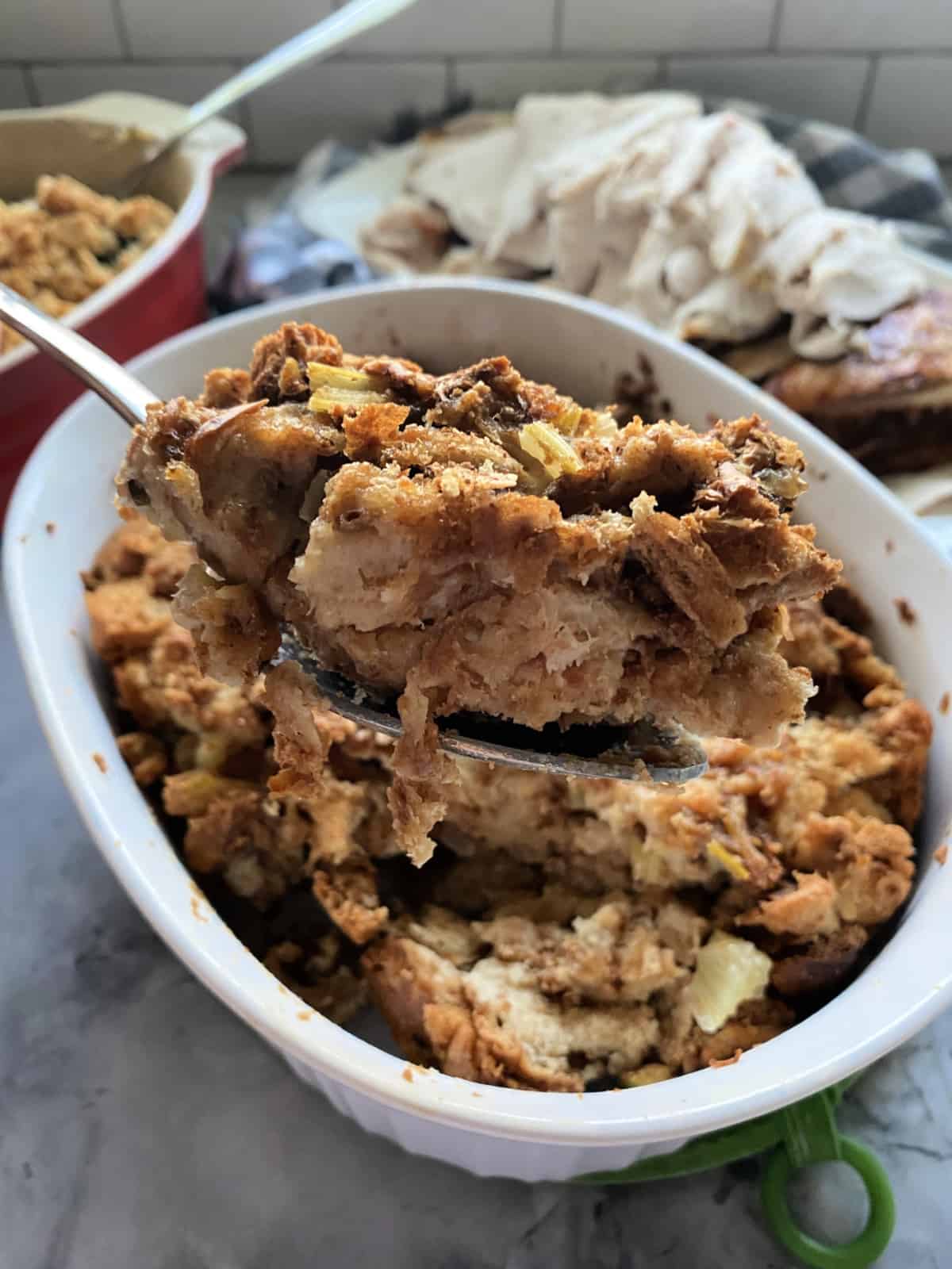 Spoon scooping bread stuffing out of a white casserole dish.