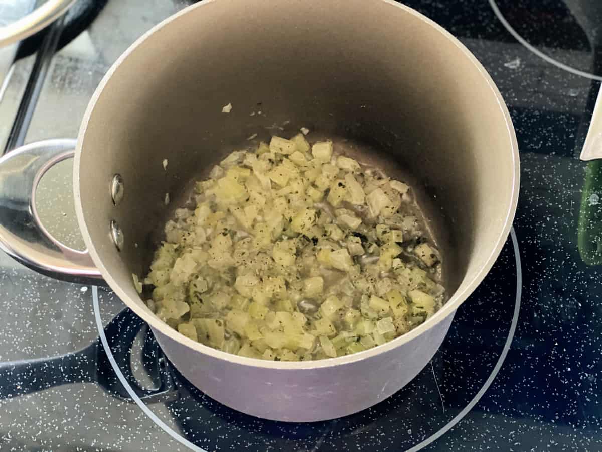 Brown pot on a glass cooktop filled with butter and celery.