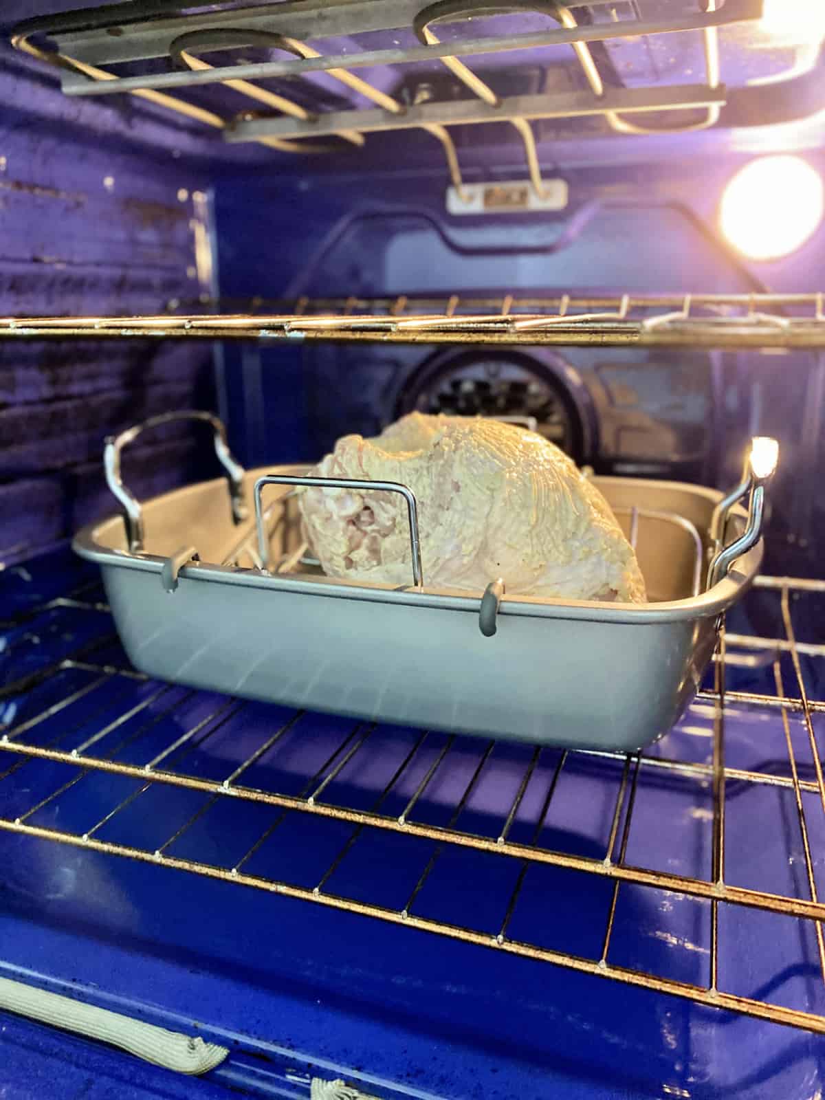 Raw chicken breast in a roasting rack inside a blue oven.