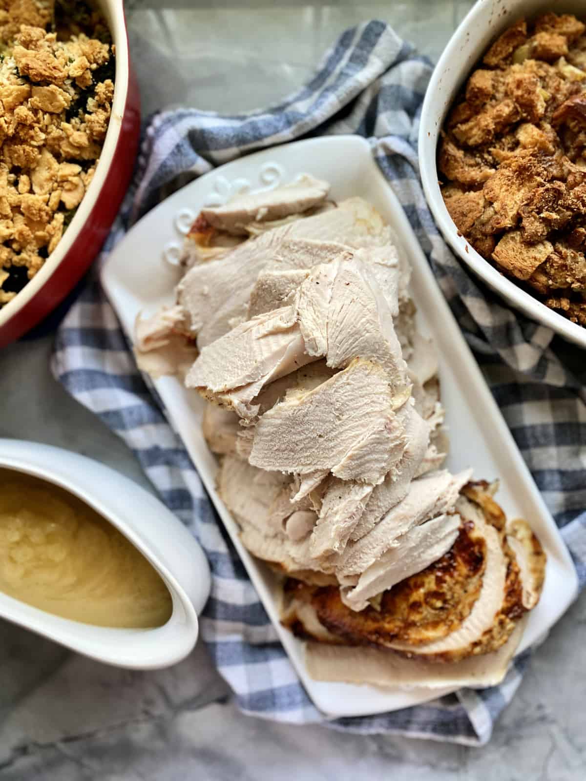 Top view of a platter of sliced turkey with sides and gravy around it.