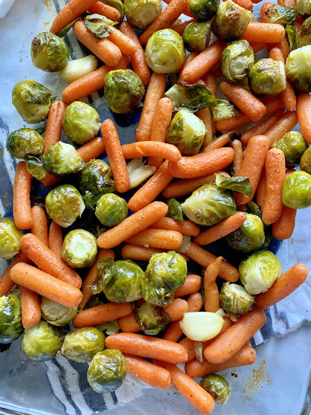 Top view of a glass baking dish filled with Roasted Brussels Sprouts cloves of garlic, and baby Carrots.