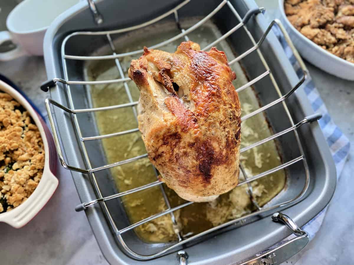 Golden roasted turkey breast in roasting pan with sides next to it.