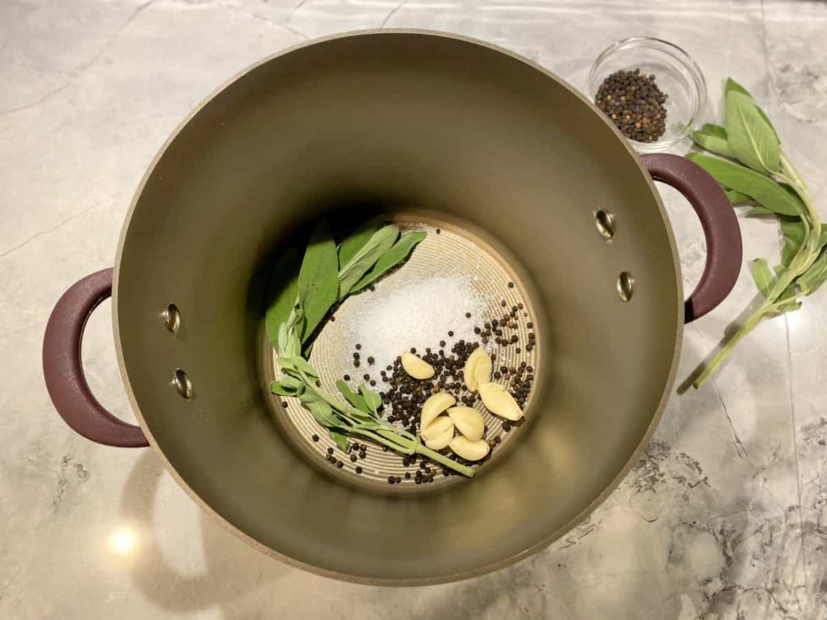 Top view of a pot filled with sage, peppercorns, salt, and garlic.