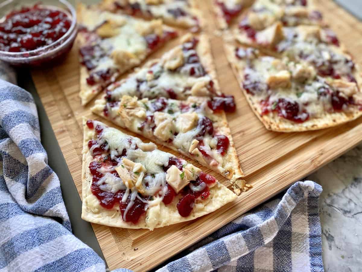 Two flatbreads on a wood cutting board with a blue and white checkered dish towel.