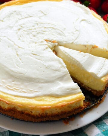 Plain cheesecake with a slice of cheesecake missing with strawberries in the background.