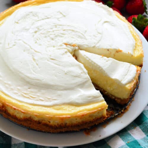 Plain cheesecake with a slice of cheesecake missing with strawberries in the background.