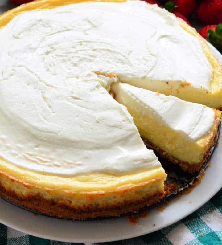 Plain cheesecake with a slice of cheesecake missing with strawberries in the background.