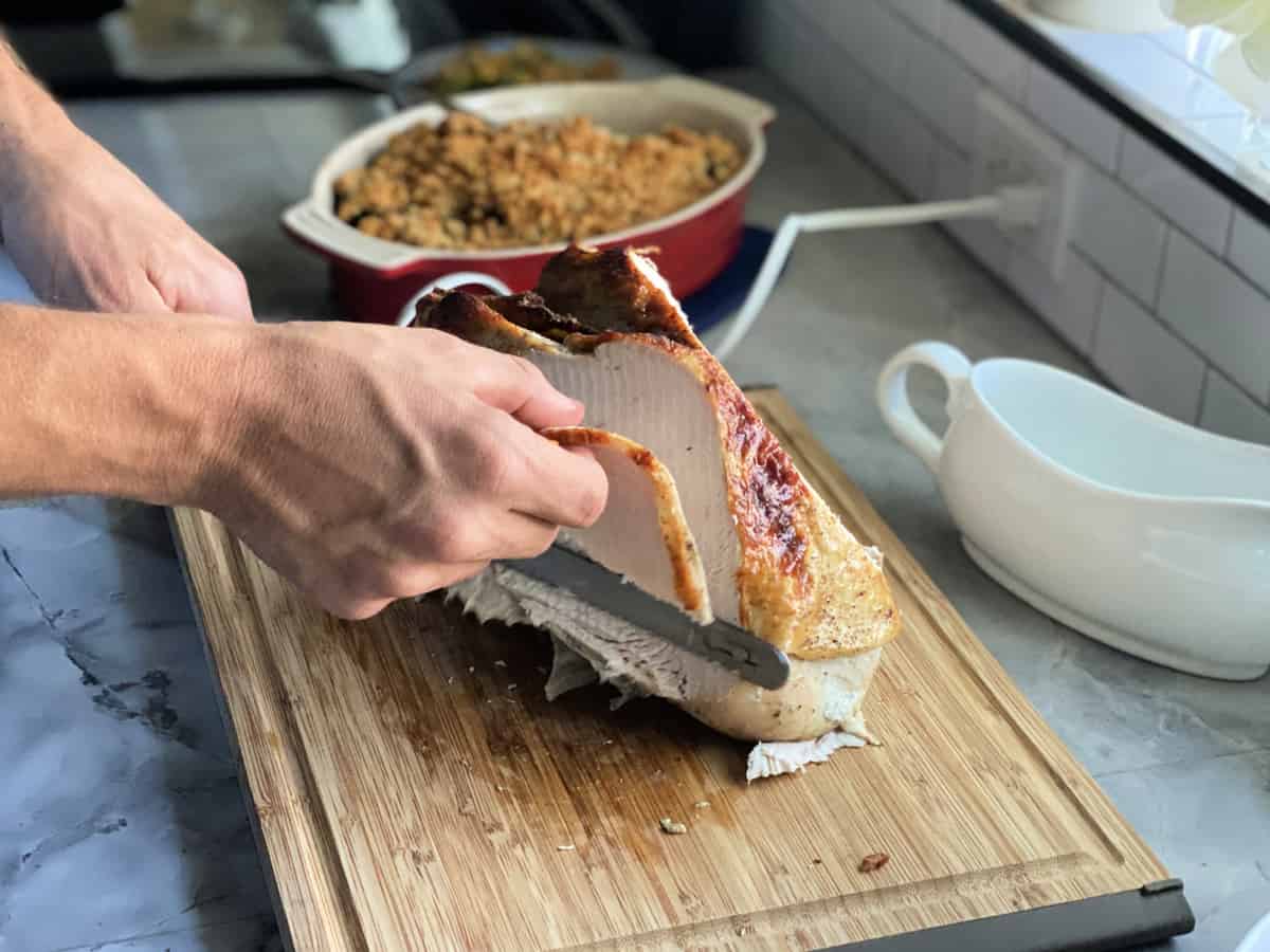 Male hamnd slicing turkey breast with an electric knife on a wood cutting board.