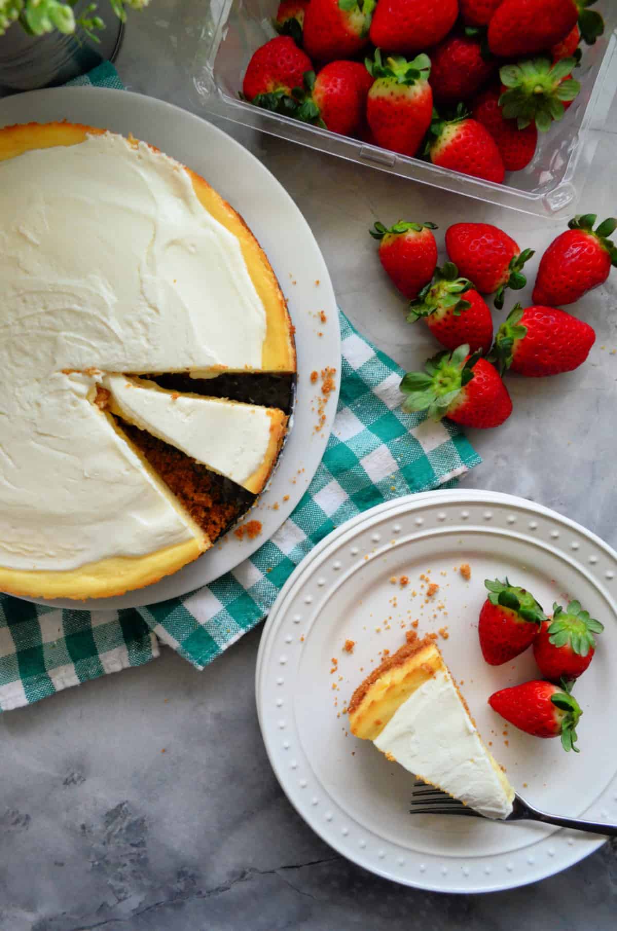 Top view of a sliced cheesecake with strawberries in a carton next to it.