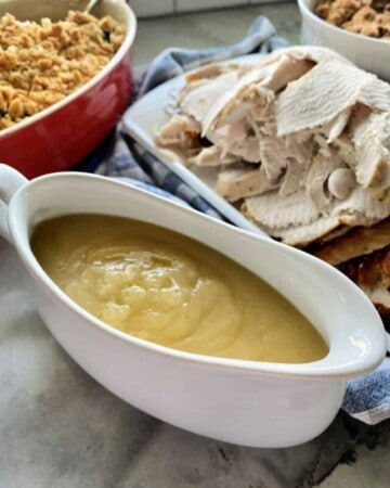 White gravy boat filled with turkey gravy with turkey and sides in the background.