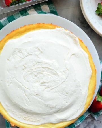 Top view of a whole cheesecake with a carton of fresh strawberries next to it.