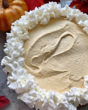 Top view of a pumpkin cheesecake pie with piped whipped cream on top.