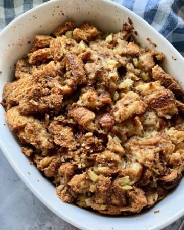 Top view of a white dish filled with bread stuffing resting on a plaid dish towel.