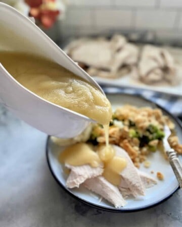 Gravy boat pouring turkey gravy on top of sliced turkey breast on a plate.