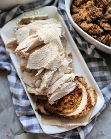 Top view of sliced turkey on a platter next to a bowl of stuffing.
