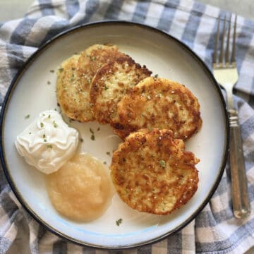 Top view of four mashed potato cakes with sour cream and applesauce on a checkerred cloth.