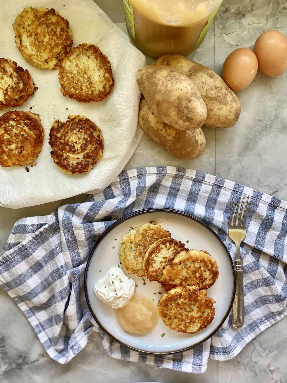 Top viiew of potato pancakes on a plate with potatoes and eggs near by.