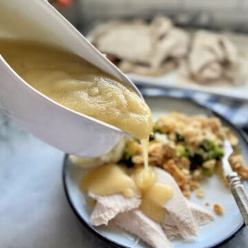 Gravy boat pouring turkey gravy on top of sliced turkey breast on a plate.
