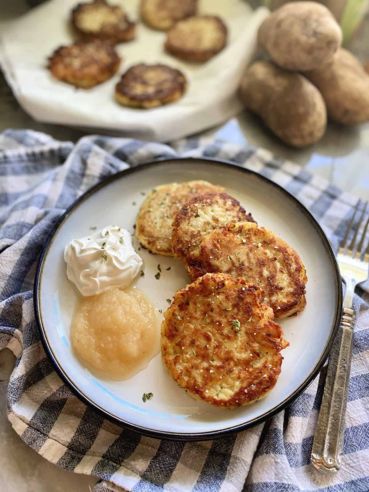 Plate of four mashed potato cakes with sour cream and applesauce next to it.