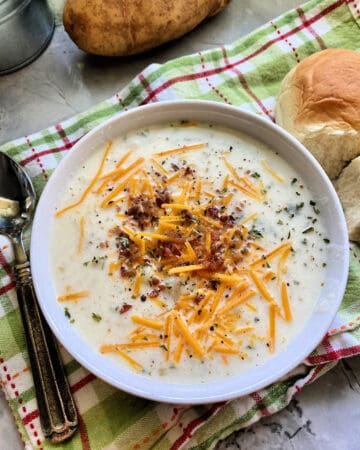 Top view of a bowl of mashed potato soup topped with bacon, cheese, and herbs.