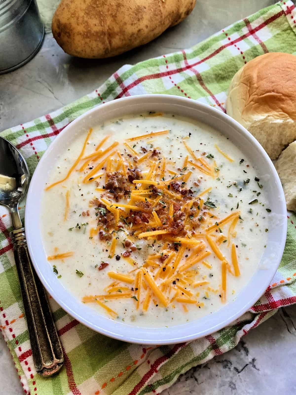 Top view of a bowl of mashed potato soup topped with bacon, cheese, and herbs.