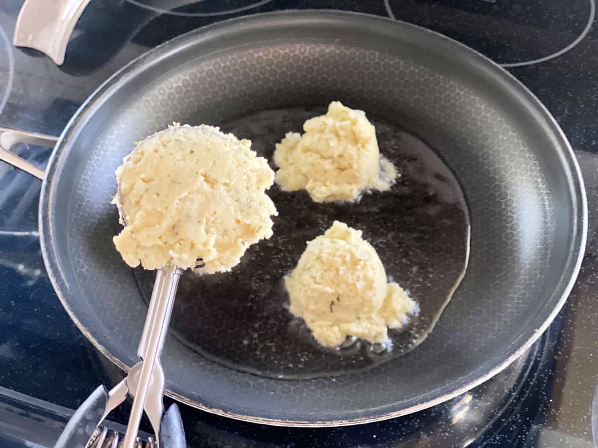 Scoop filled with mashed potatoes with two scoops of mashed potatoes in background in frying pan.