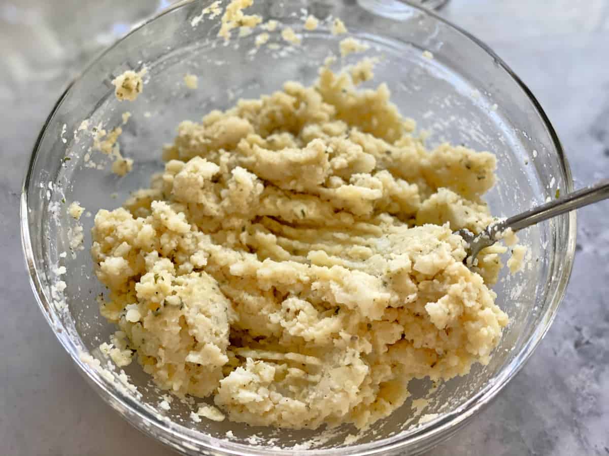 Glass bowl of mashed potatoes mixed with a fork.