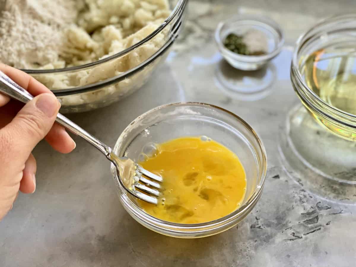 Female hand mixing eggs in a glass bowl with a fork.