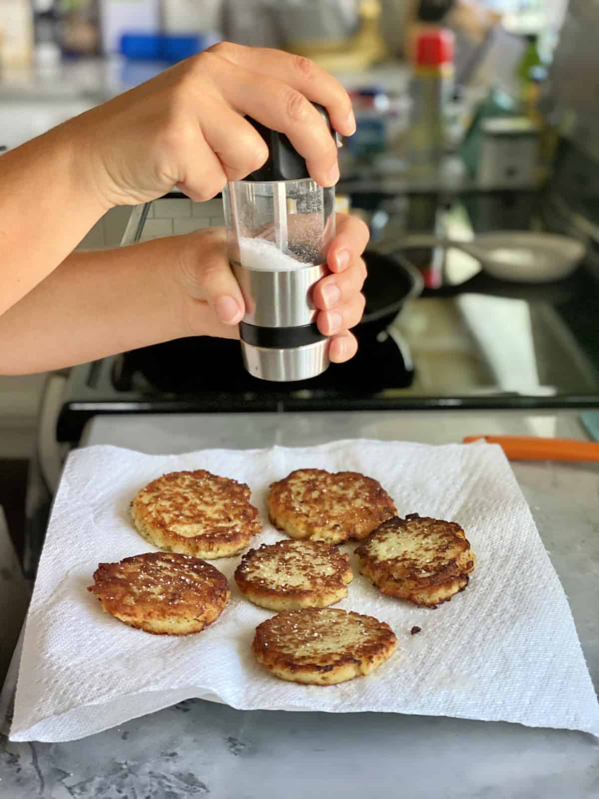 Female hand grinding salt on top of potato cakes on a paper towel lined plate.