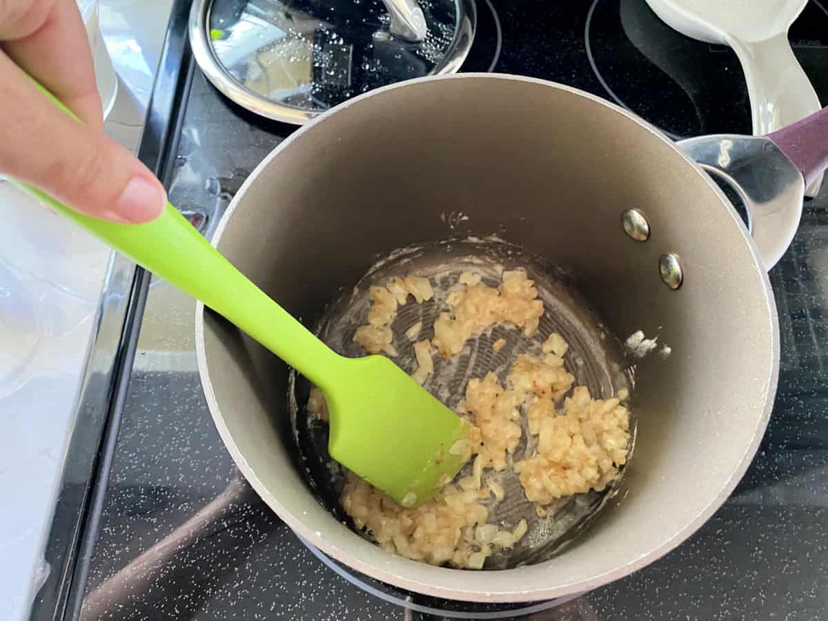 Female hand using green spatular mixing onions and butter together.