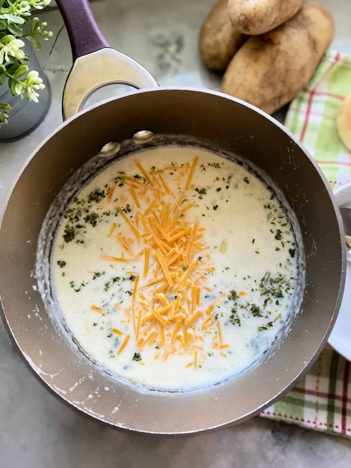Sauce pan filled with potato soup topped with cheese and parsley.