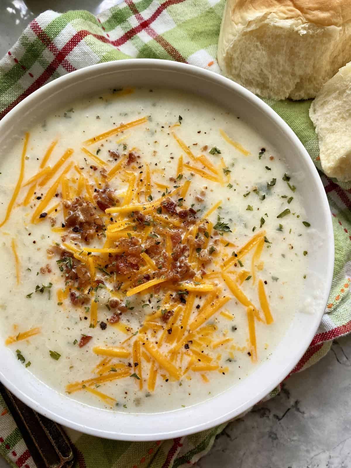 Top view of a bowl of potato soup with bacon, cheese, and parsley.