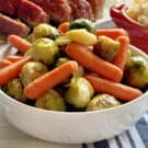 White bowl filled with roasted baby carrots and brussels sprouts.